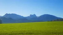 Blick auf eine Wiese, im Hintergrund Berge und blauer Himmel
