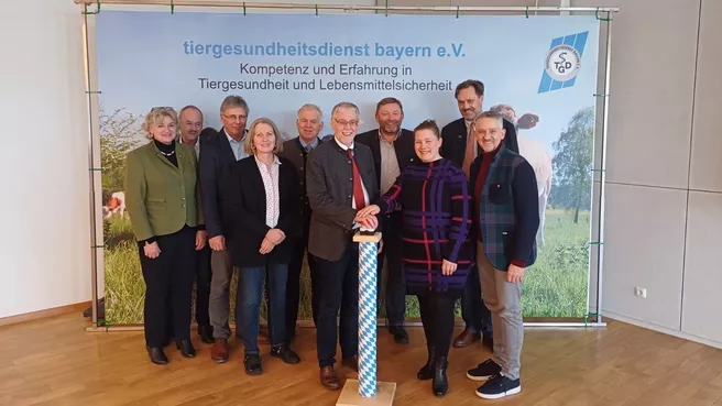 Project participants stand in front of the banner of the Bavarian Animal Health Service, two people hold their hands on a symbolic start button